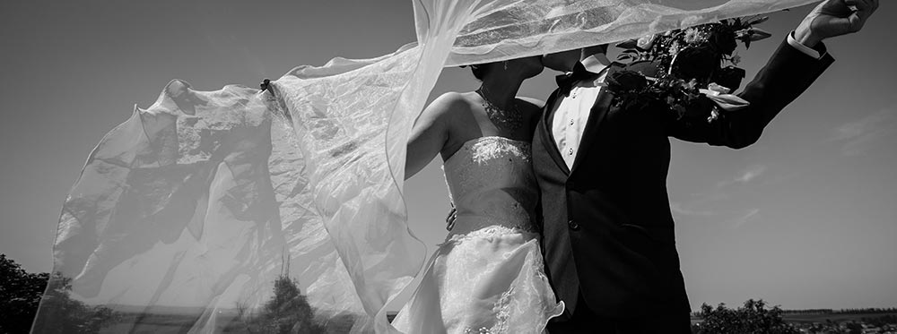 Photo de mariage noir et blanc : Couple s'embarssant derrière le voile de la mariée